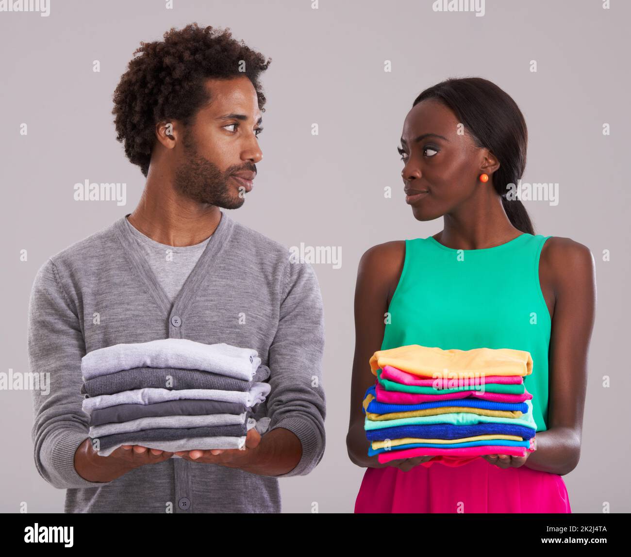 Fashion faceoff. Studio shot of a young man and woman each holding a neatly folded pile of clothes. Stock Photo