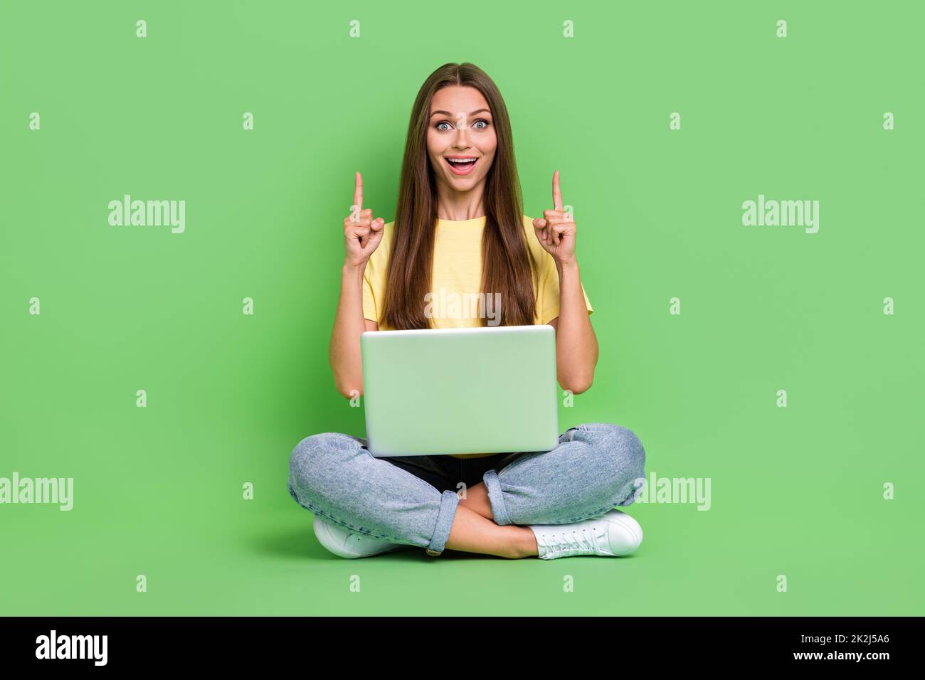 Photo of astonished cute lady sit arm demonstrate empty space offer use modern device gadget netbook isolated on green color background Stock Photo