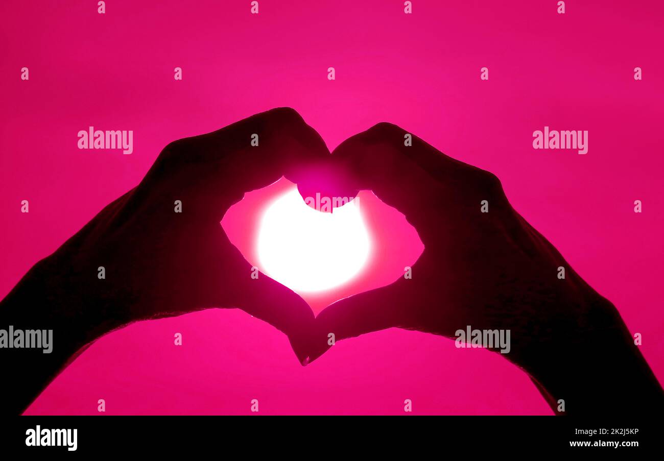 Pop art style silhouette of hand making heart sign to the bright sun on ruby sky Stock Photo