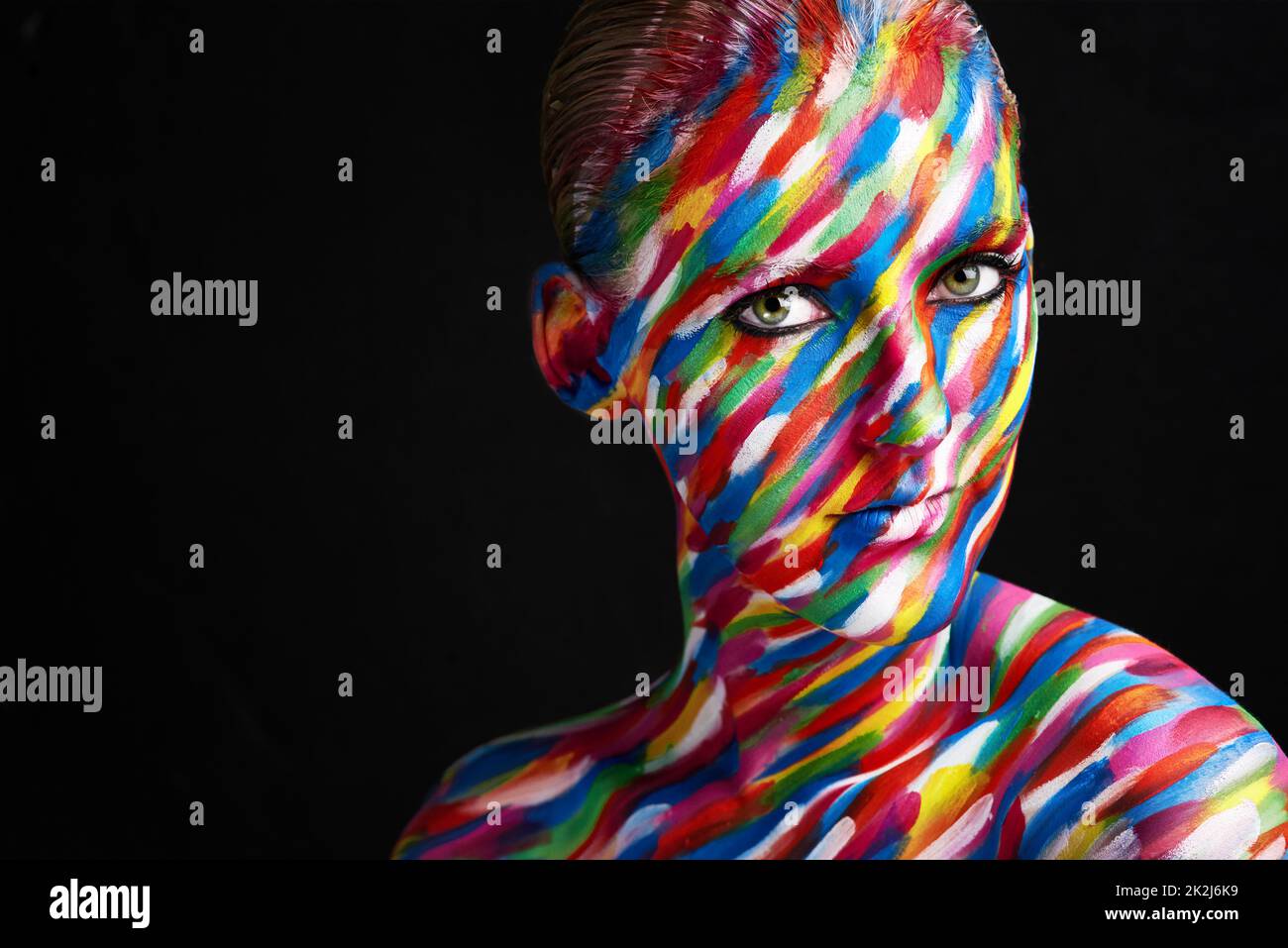 Makeup is an art. Studio shot of a young woman posing with brightly colored paint on her face against a black background. Stock Photo