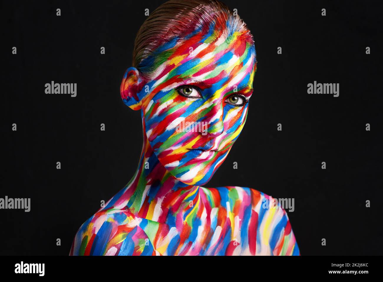 Eye catching, eye popping colorful beauty. Studio shot of a young woman posing with brightly colored paint on her face against a black background. Stock Photo