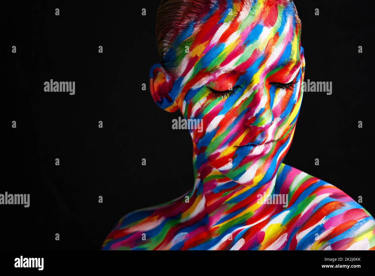 She looks good in every color. Studio shot of a young woman posing with brightly colored paint on her face against a black background. Stock Photo
