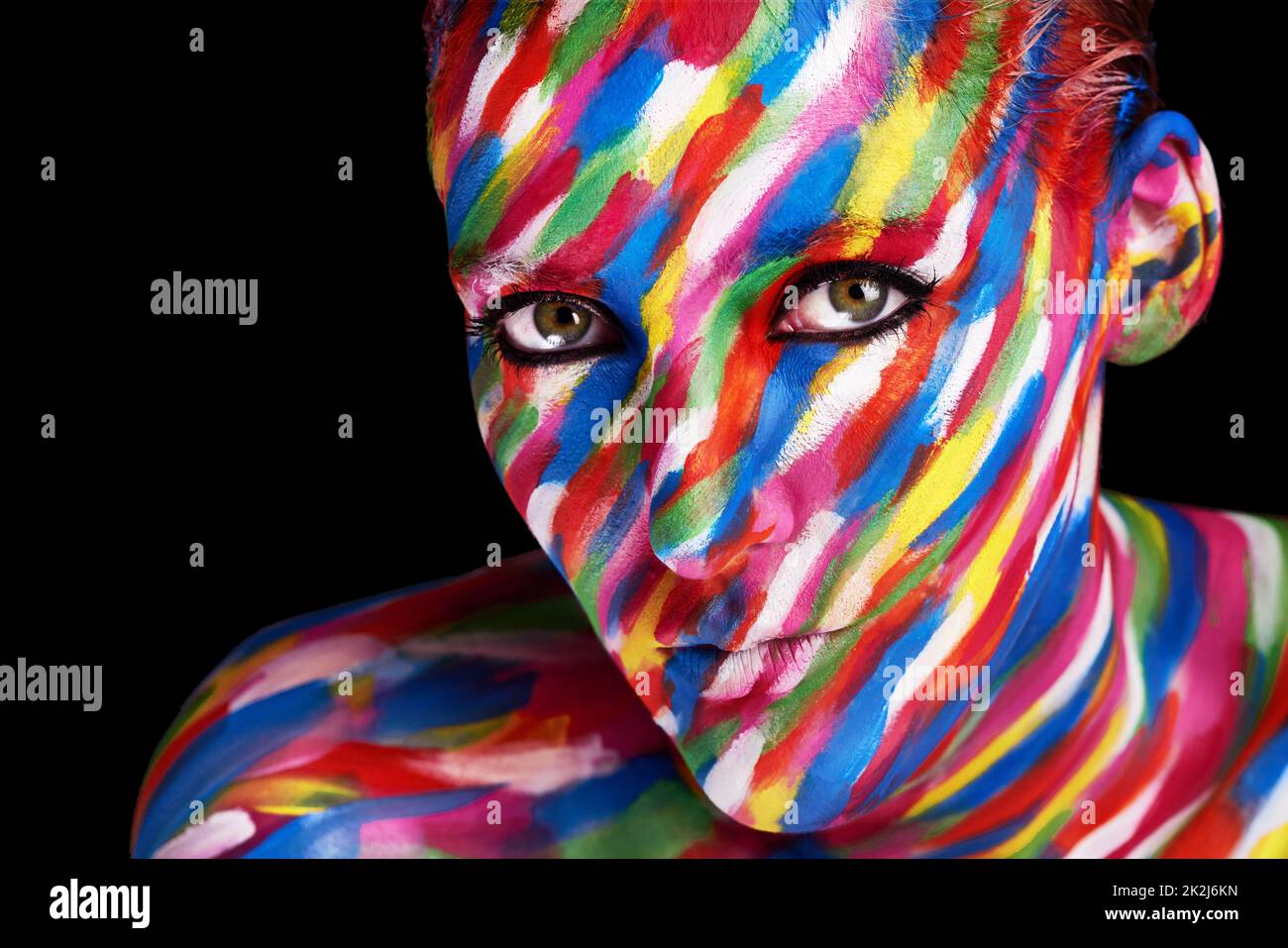 Live life vividly. Studio shot of a young woman posing with brightly colored paint on her face against a black background. Stock Photo