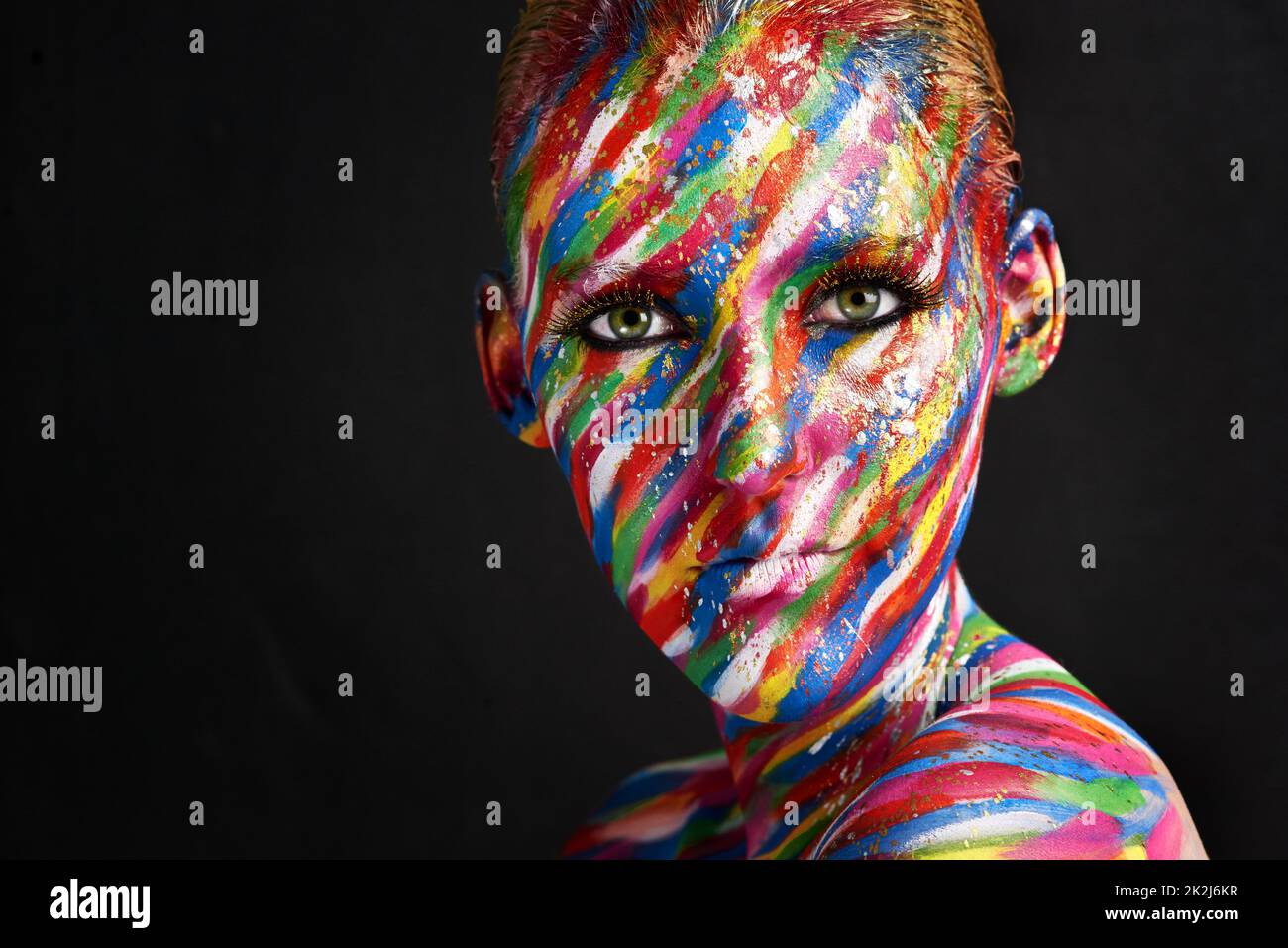 She finds beauty in color. Studio shot of a young woman posing with brightly colored paint on her face against a black background. Stock Photo