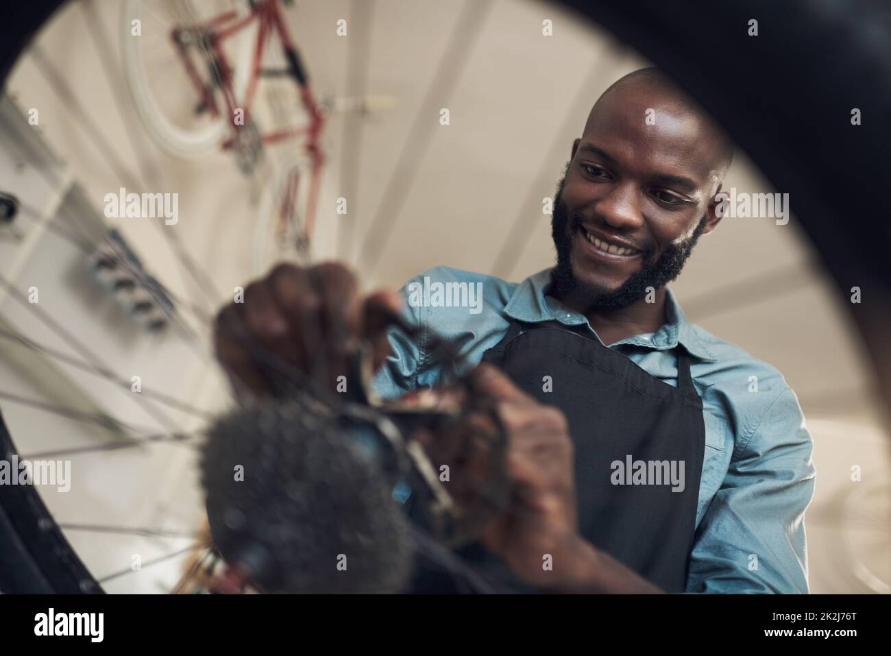This bike really needed a new part. Low angle shot of a handsome young man standing alone in his shop and repairing a bicycle wheel. Stock Photo