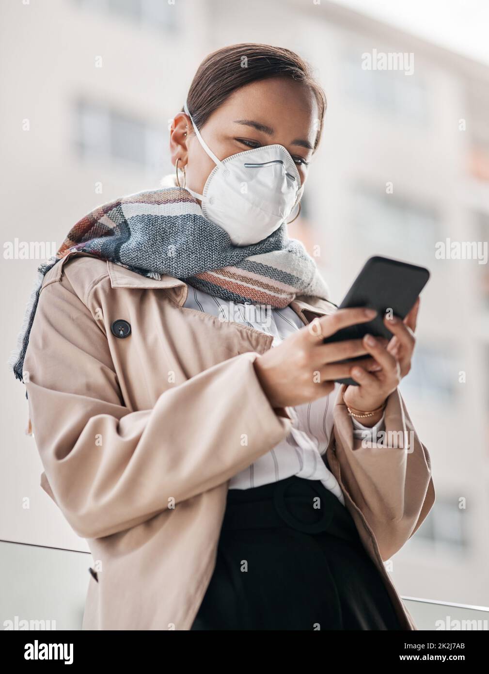 Social interaction is still doable with the help of technology. Shot of a young woman wearing a mask and using a smartphone on the balcony at home. Stock Photo