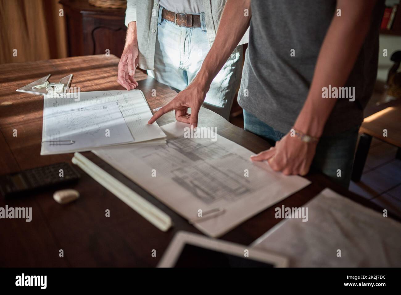 Going over the specs together. Shot of an unidentifiable father and his son working on a design for their family business at home. Stock Photo