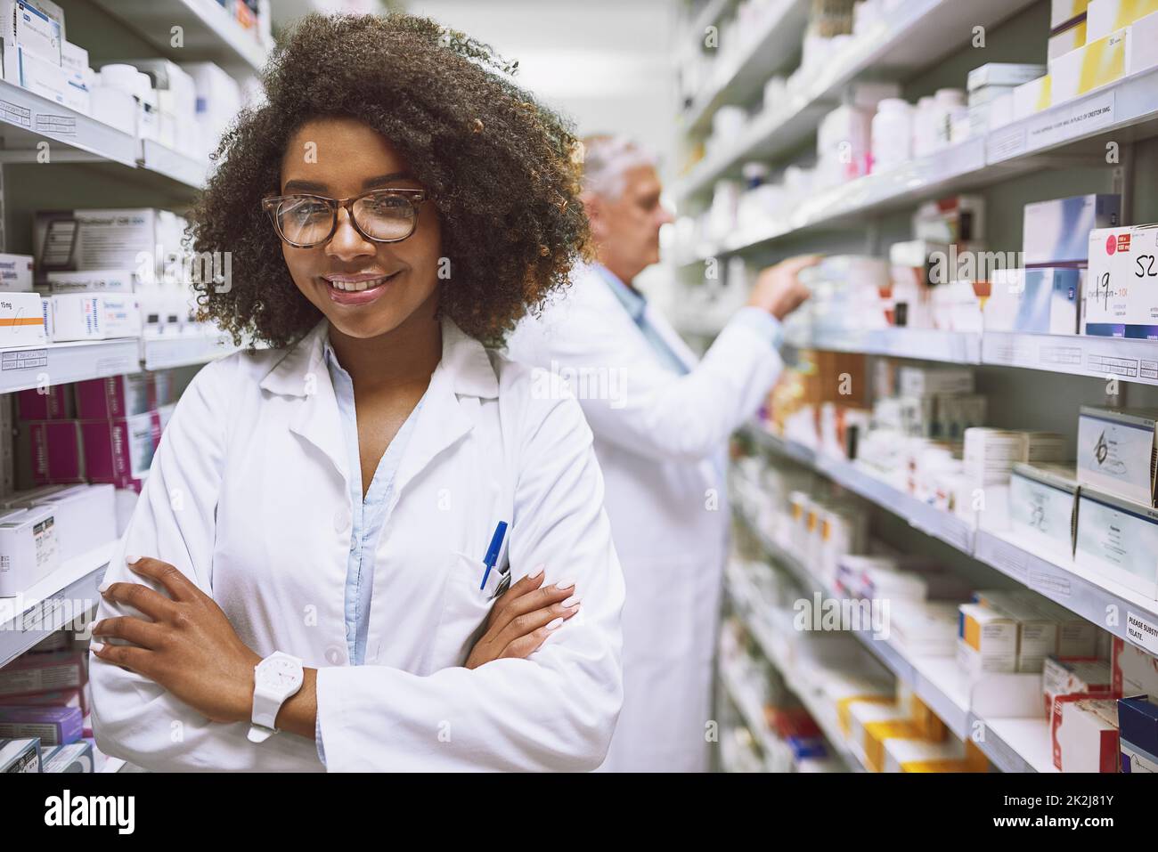 We have what you need right here. Portrait of a cheerful young female pharmacist standing with arms folded while looking at the camera in a pharmacy. Stock Photo