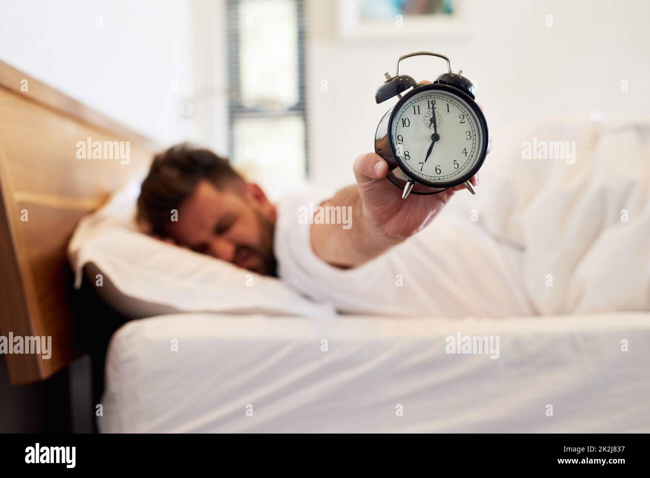 Time to face the day. Cropped shot of a young man holding up an alarm clock while waking up from bed at home. Stock Photo