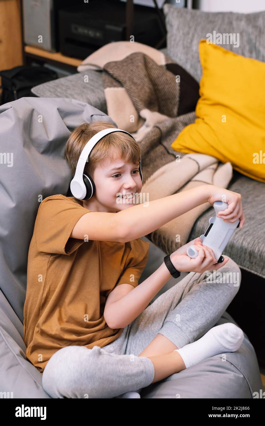 Teen boy actively and recklessly playing video game with joystick sitting on frameless beanbag chair Stock Photo