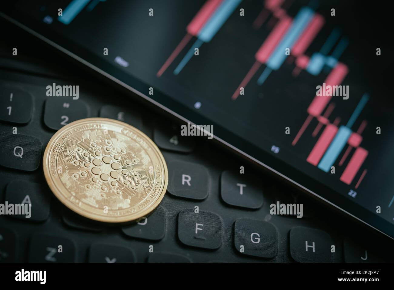 Golden Cardano (ADA) cryptocurrency coin with candle stick graph chart, laptop keyboard, and digital background. Stock Photo