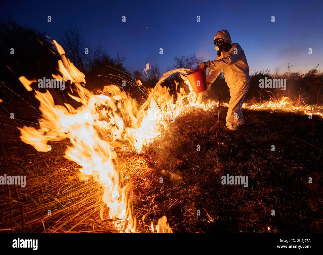 Fireman extinguishing fire in field with blue night sky on background