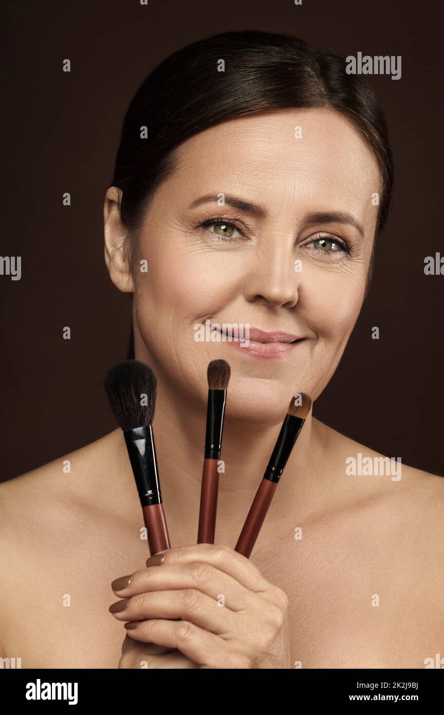 Beautiful middle aged woman with a makeup brushes on brown background Stock Photo
