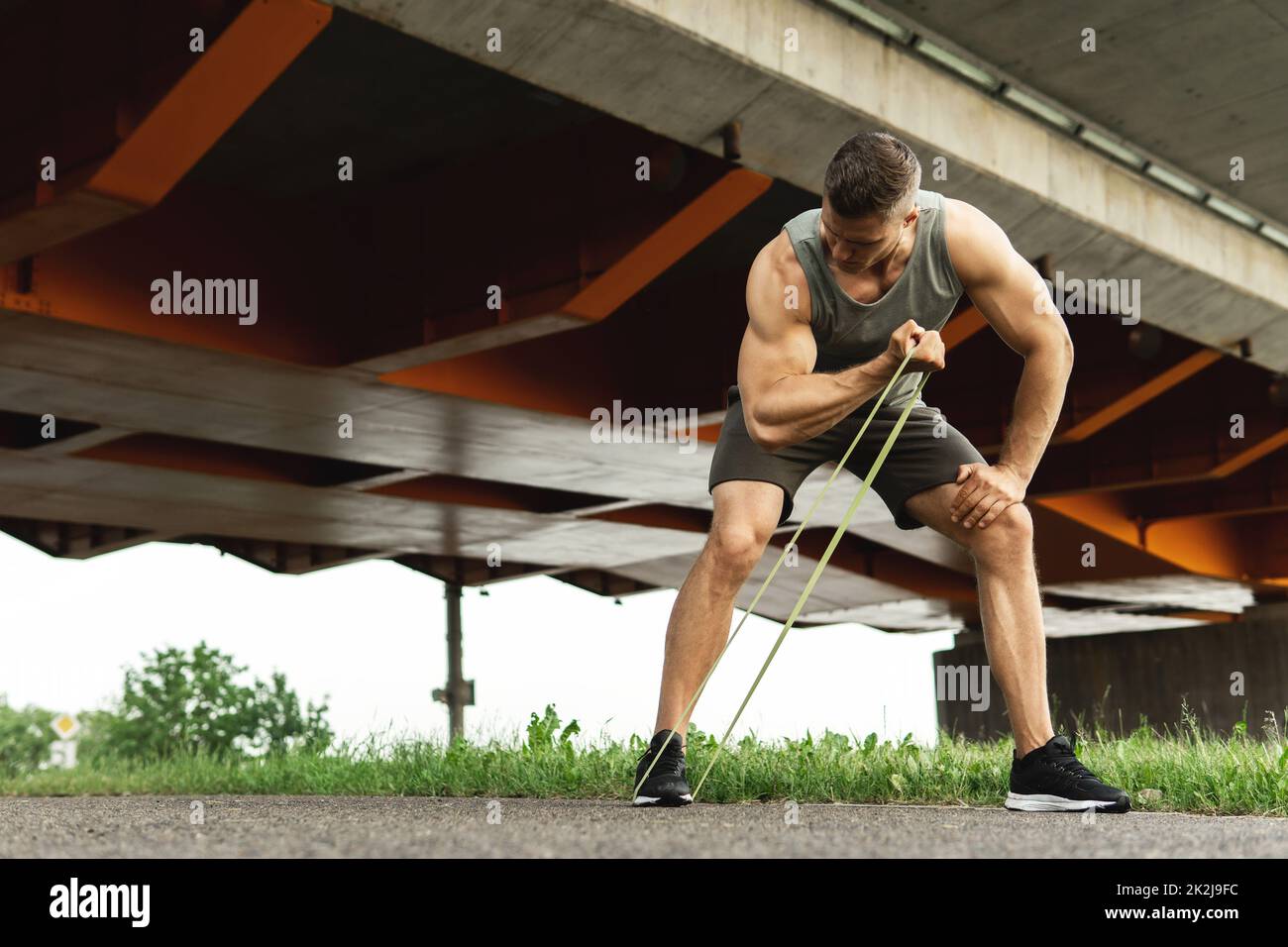Muscular man during workout with a resistance rubber bands on a stree