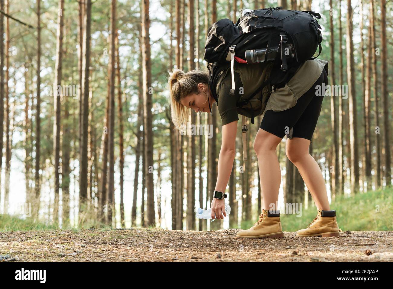 Female hiker collecting plastic waste in green forest Stock Photo