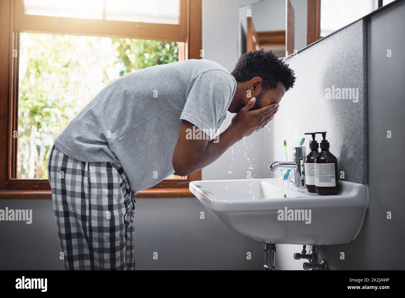 Freshening up. Cropped shot of a handsome young man washing his face in the bathroom at home. Stock Photo