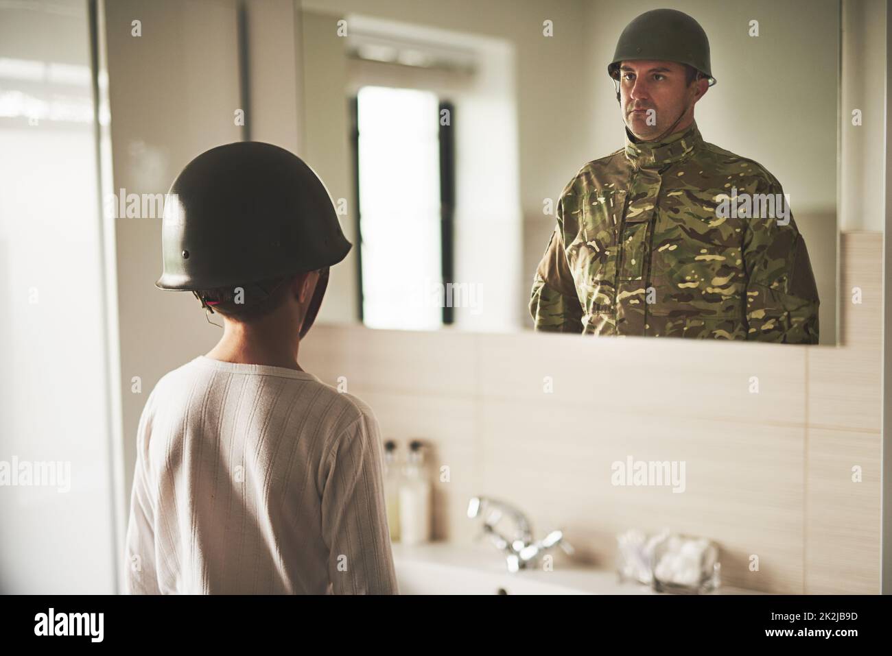 Daddy, come home. Rearview shot of a young boy wearing an army helmet seeing his fathers reflection in the mirror. Stock Photo