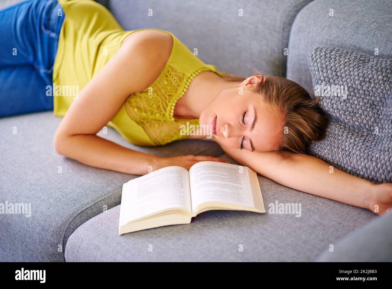 Nowhere more relaxing than home.... Shot of a young woman sleeping beside a book on her sofa at home. Stock Photo
