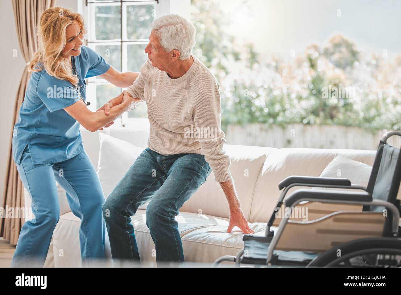 Shot of a young nurse helping her elderly male patient stand up Stock