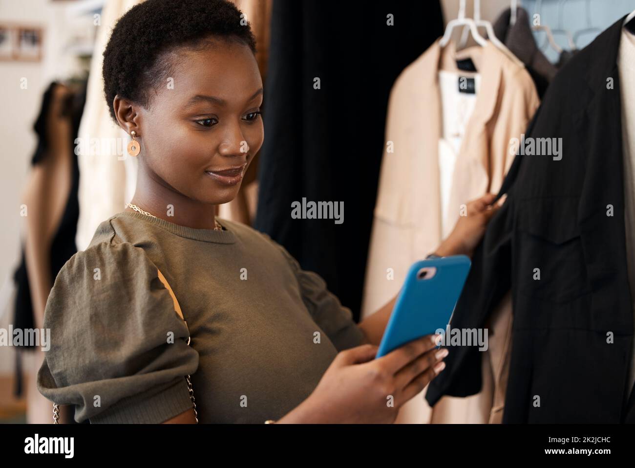 Its a womans duty to share a good bargain. Shot of a beautiful young woman using her cellphone while shopping for clothing at her favourite boutique. Stock Photo