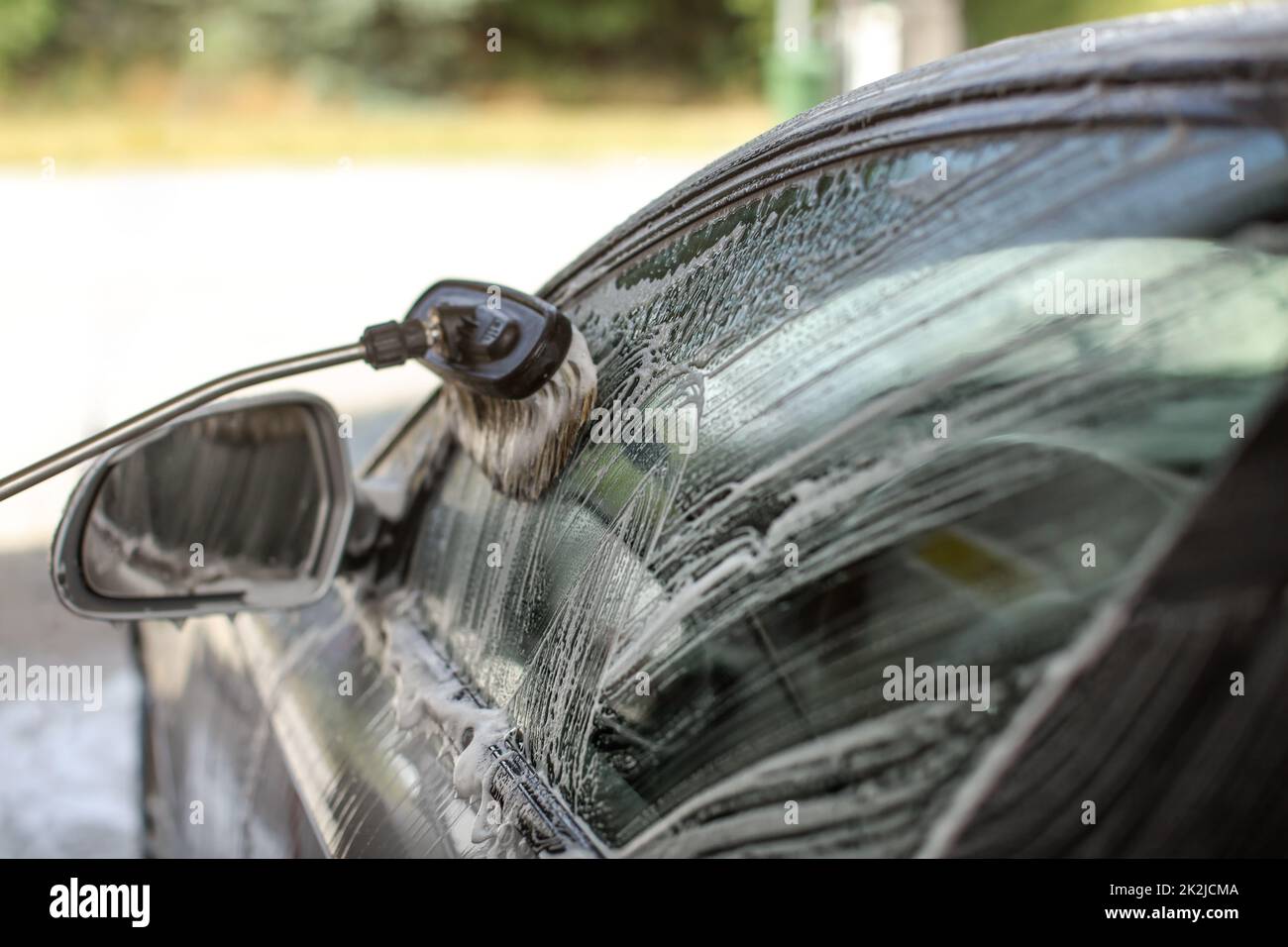 Side of a car washed in self serve carwash. Brush cleaning glass, strokes visible in shampoo foam. Stock Photo