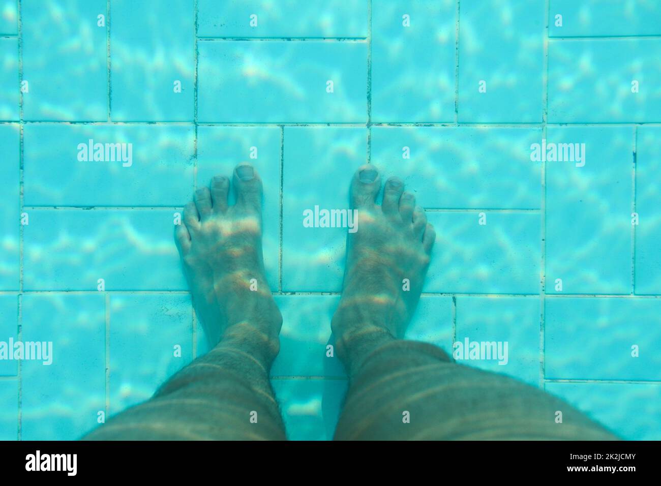 Underwater photo, bottom of swimming pool with blue tiles, man legs standing on it. Stock Photo