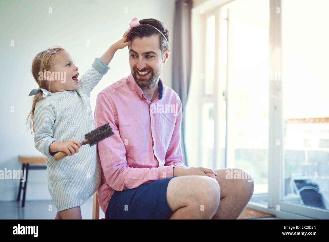 Future hairstylist in the making. Shot of an adorable little girl brushing her fathers hair at home. Stock Photo