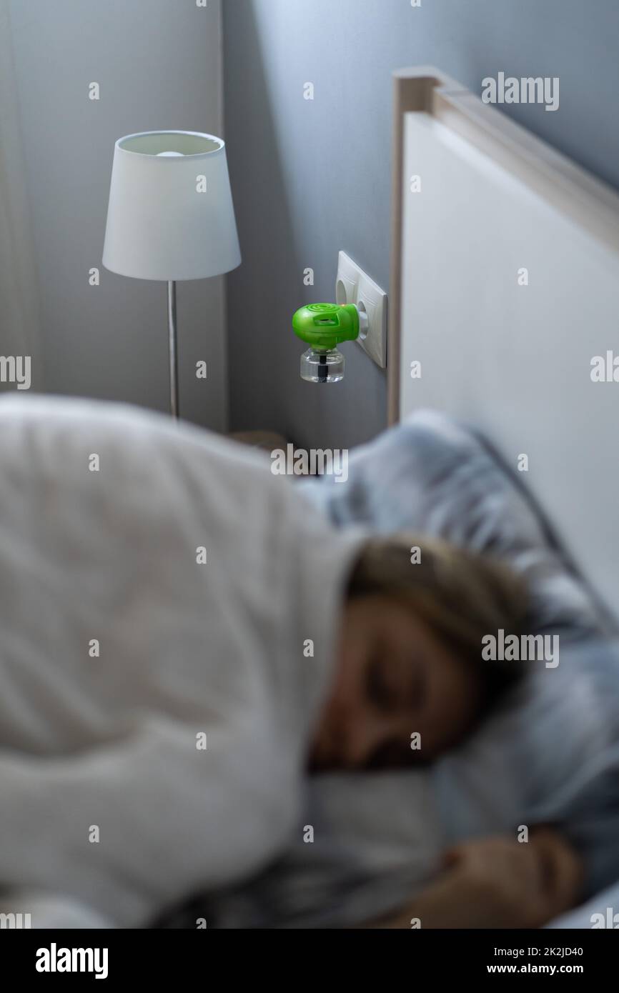 Female sleep in bed next to an electric fumigator in socket to protect against biting insects Stock Photo