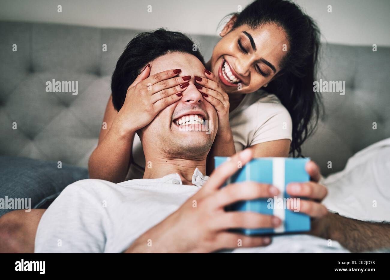 Are you ready to see what I got you. Shot of a woman covering her boyfriends eyes while surprising him with a gift. Stock Photo