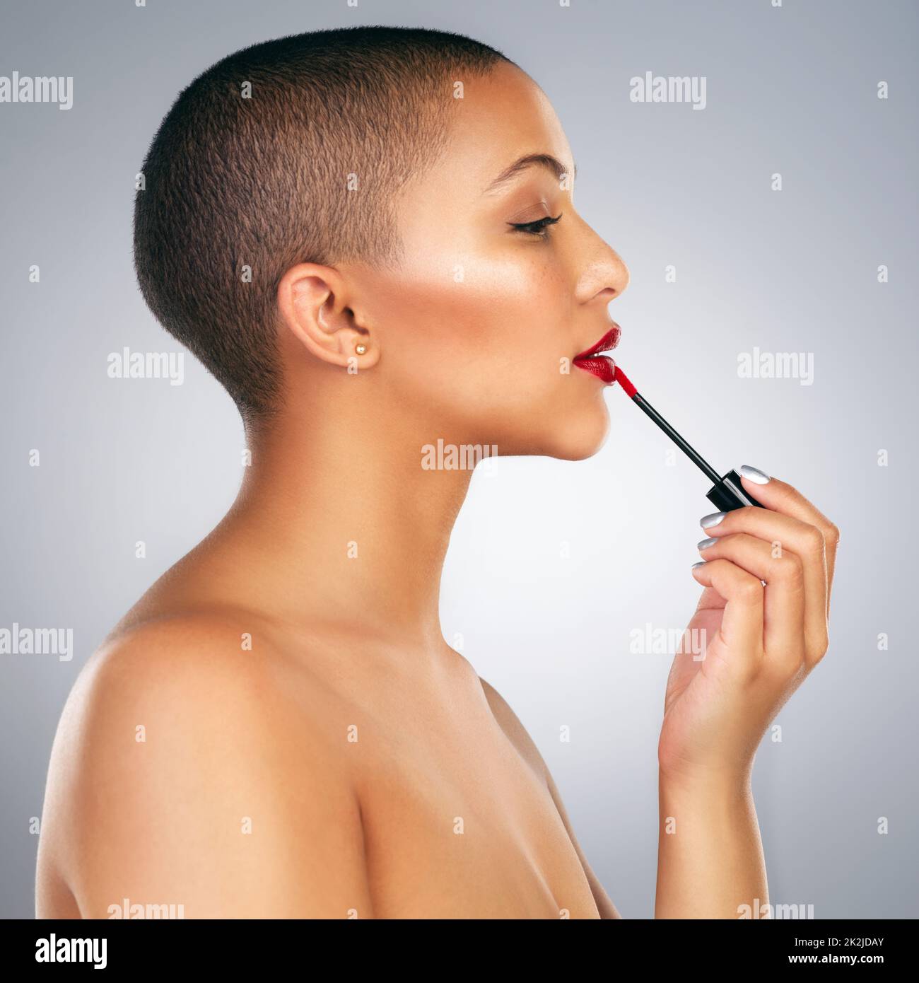 I like my lips bold. Studio shot of a beautiful young woman applying red lipstick against a grey background. Stock Photo