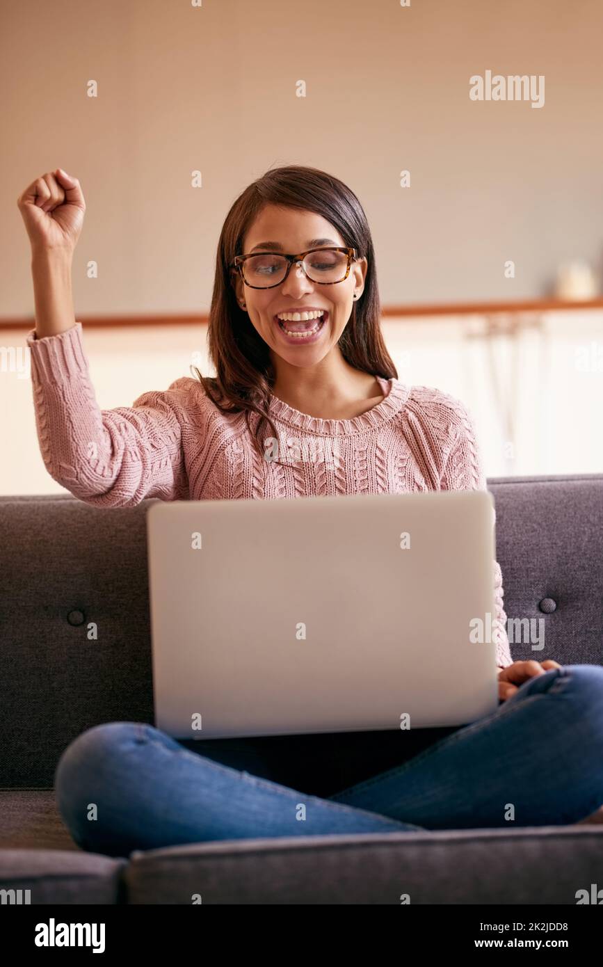 Ill be spending my weekend online. Shot of an attractive young woman using a laptop on the sofa at home and cheering. Stock Photo