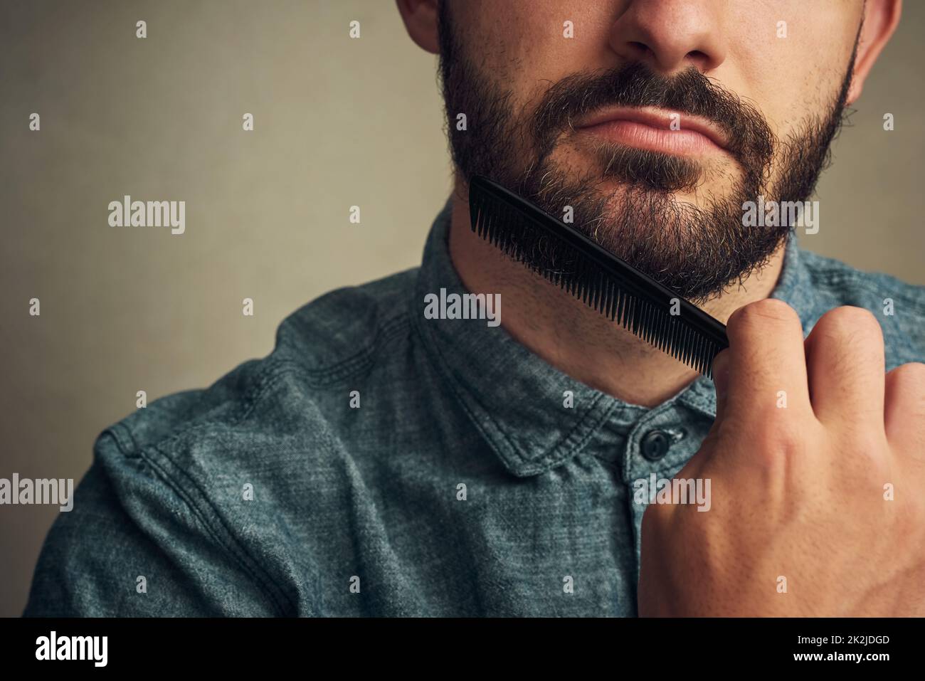They cant resist the beard. Cropped shot of a handsome young man combing his beard against a grey background. Stock Photo
