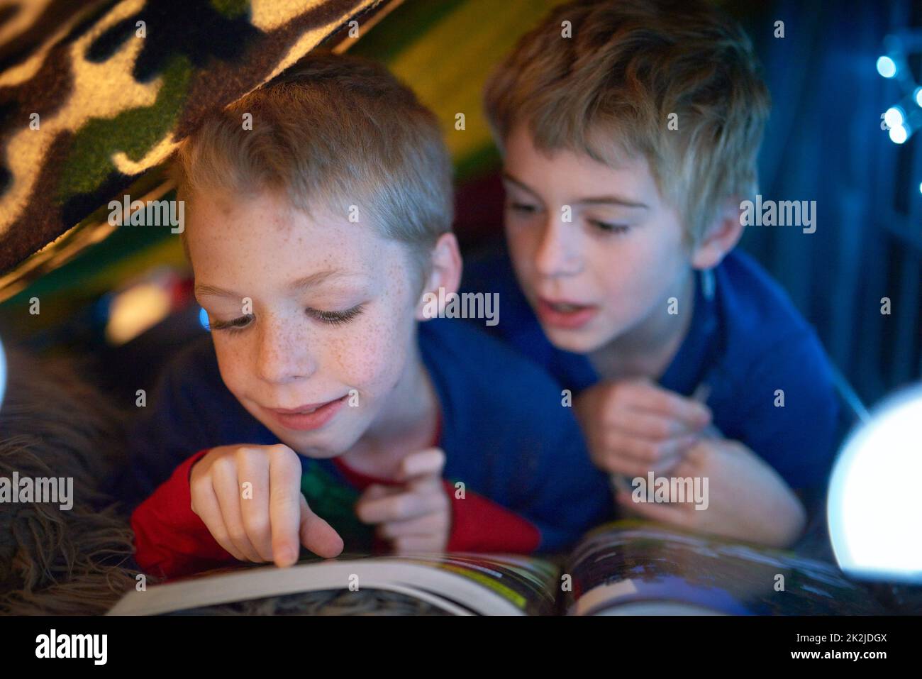 He enjoys reading bedtime stories. Shot of two little brothers reading a bedtime story under their fort. Stock Photo