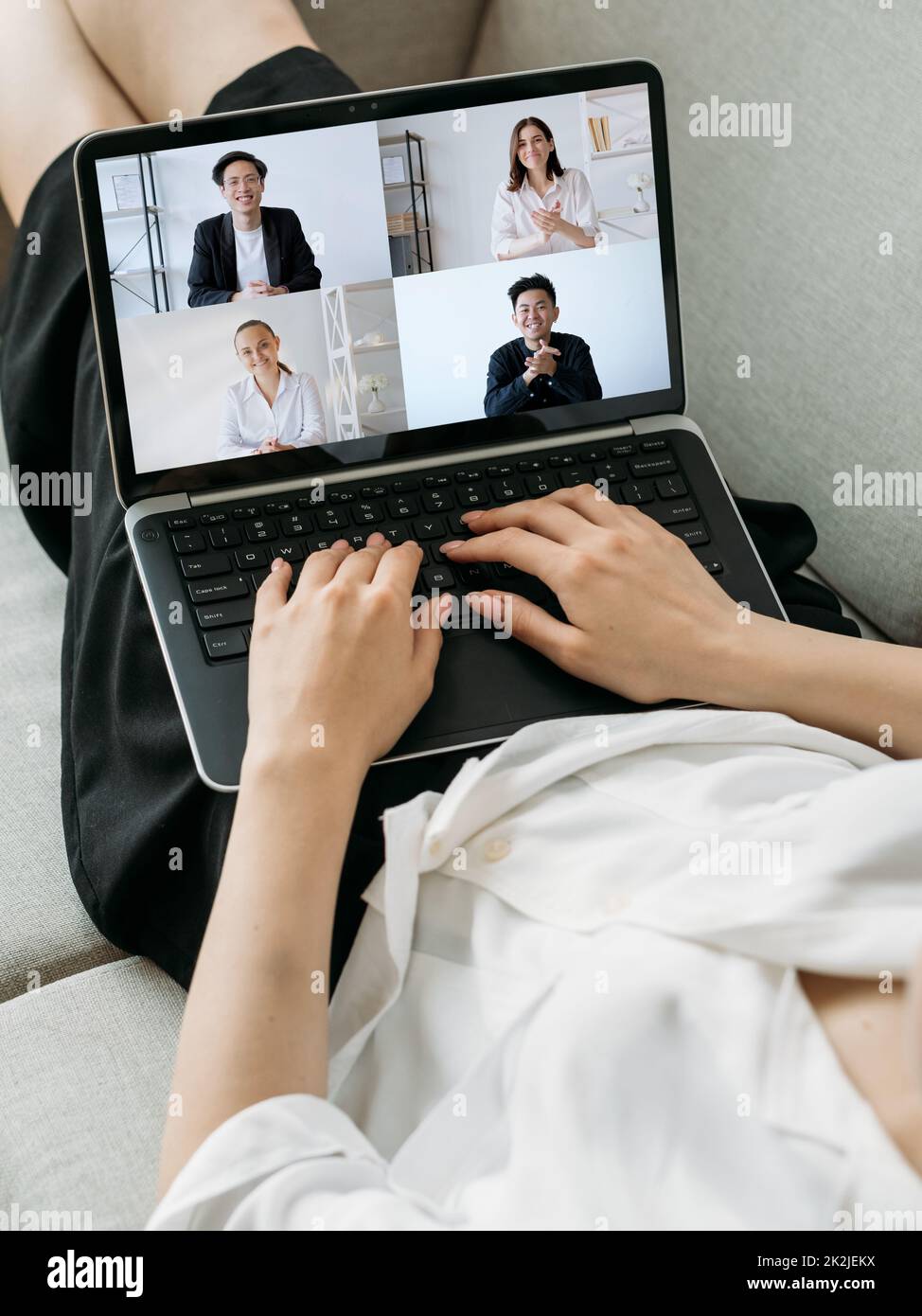 Video call. Global telework. Wfh internet conference. Relaxed woman using laptop on couch working from home online with diverse business team on scree Stock Photo