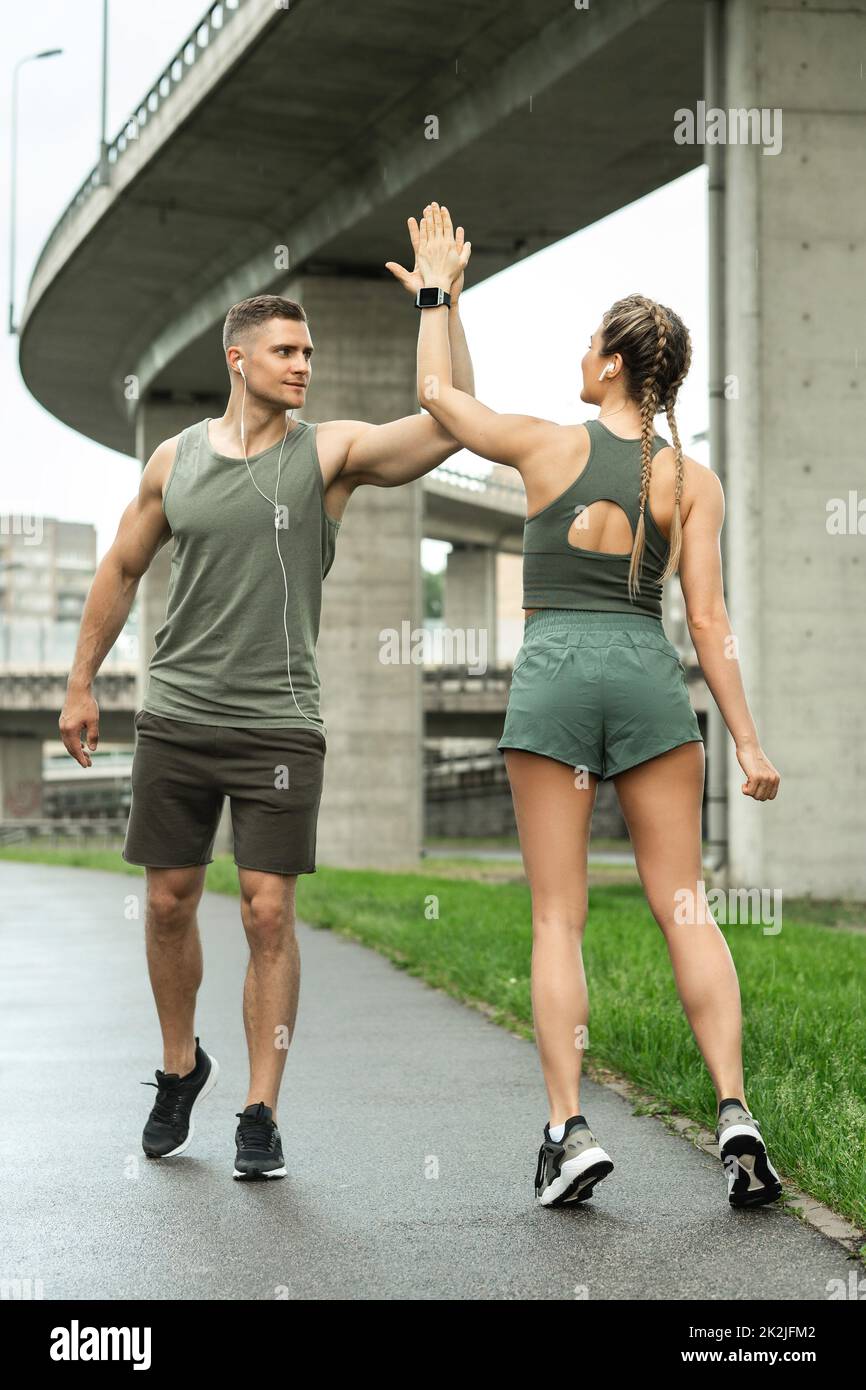 Two athletic people greeting each other with high five gesture during jogging workout Stock Photo