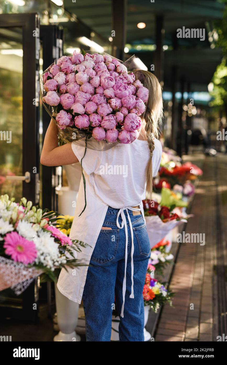 Woman florist with a heap of pink peony flowers in her little flower ...