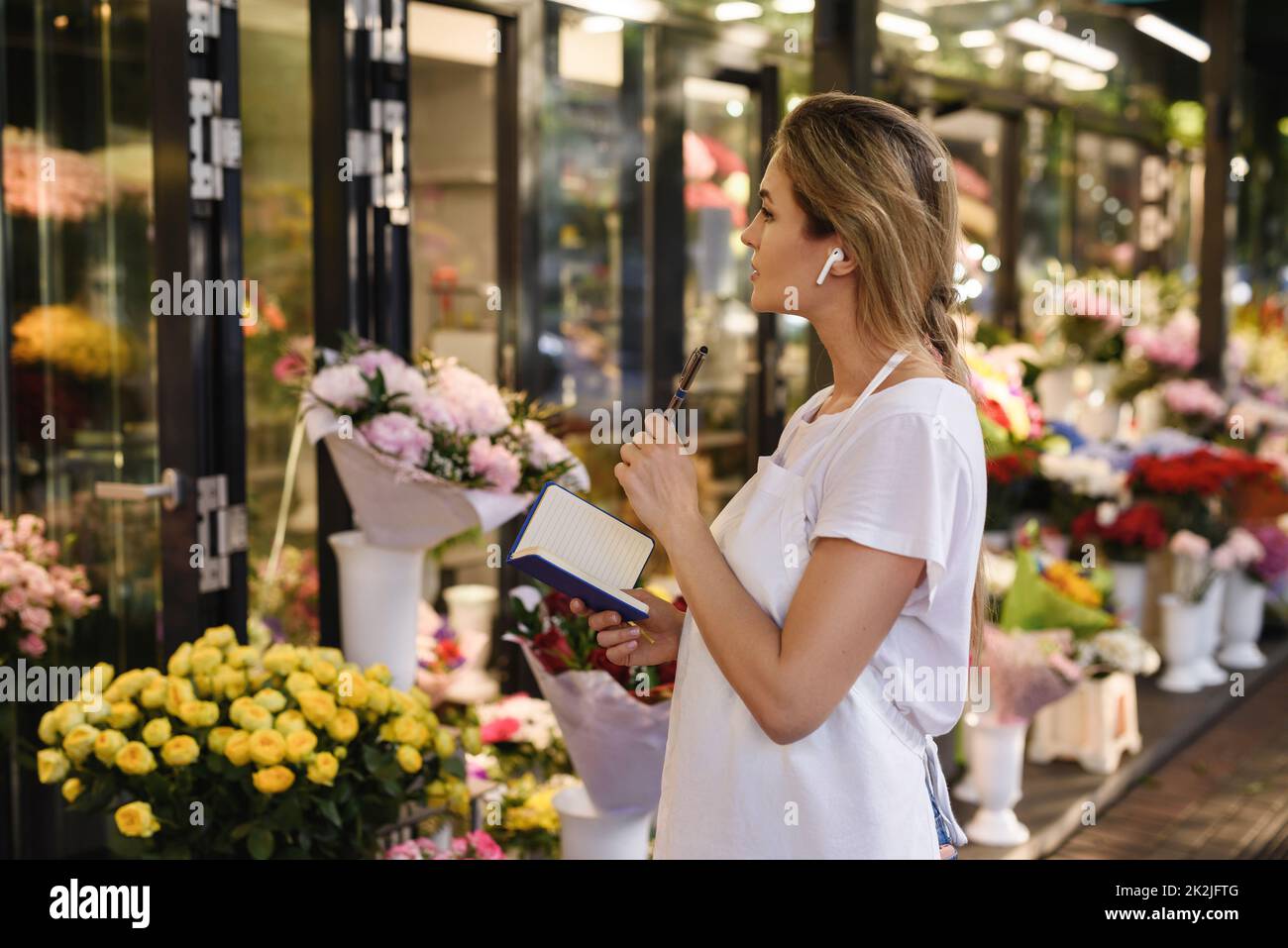 Woman florist taking new order by phone using wireless earbuds in her
