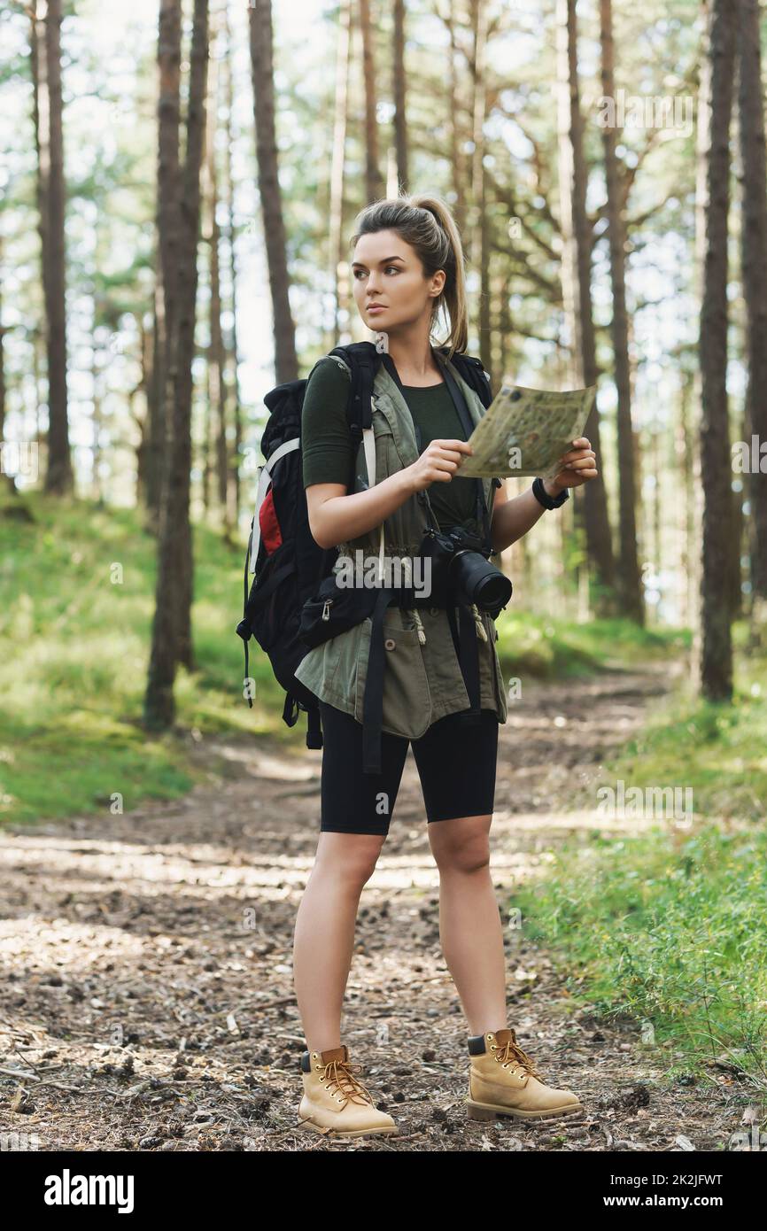 Female hiker with big backpack using map for orienteering in the forest Stock Photo
