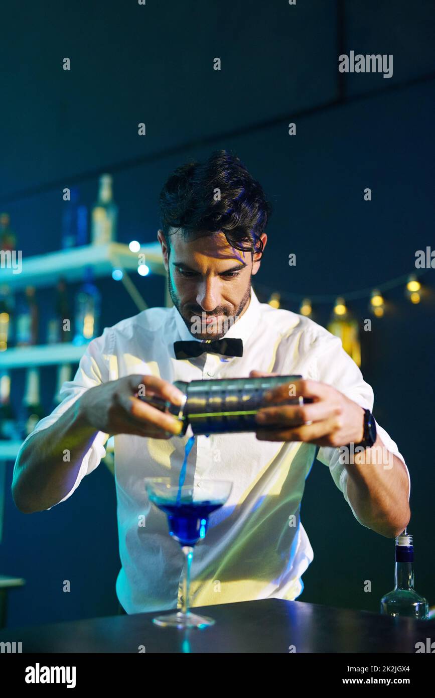 Shaken, stirred, served. Shot of a handsome young barman pouring a cocktail into a glass in a night club. Stock Photo