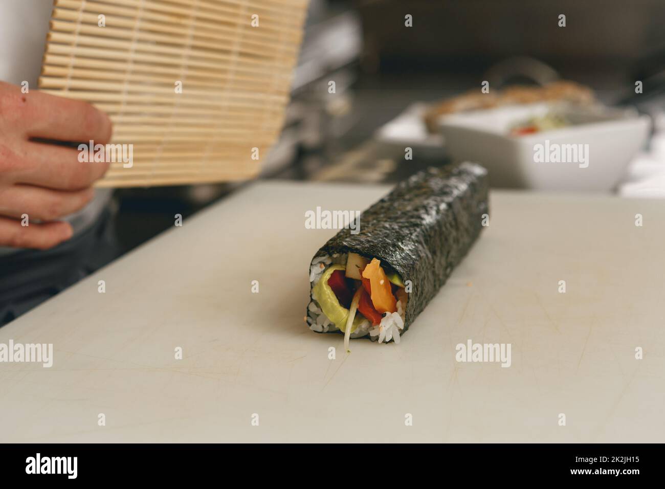 Closeup of Chef hands rolling up sushi on bamboo mat in kitchen of restaurant Stock Photo