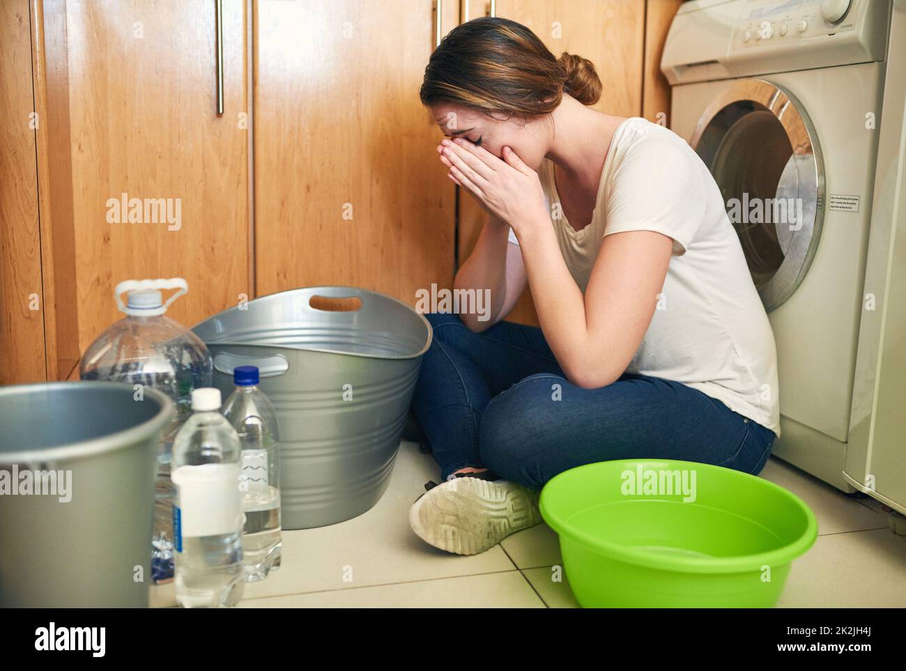 Feeling stressed about the water crisis. Shot of a beautiful young woman crying on the floor in the kitchen at home. Stock Photo