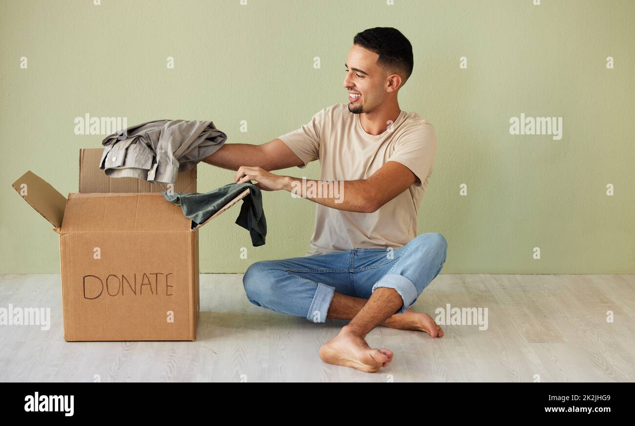 Donating some of my old clothes. Shot of a young man putting clothes into a donation box at home