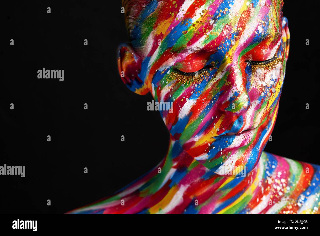 Mega bold makeup. Studio shot of a young woman posing with brightly colored paint on her face against a black background. Stock Photo