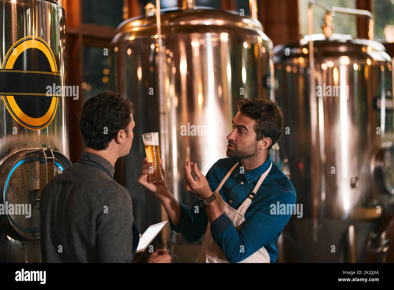 Its all about the flavor. Shot of two young working men doing inspection of their beer making machinery inside of a beer brewery during the day. Stock Photo