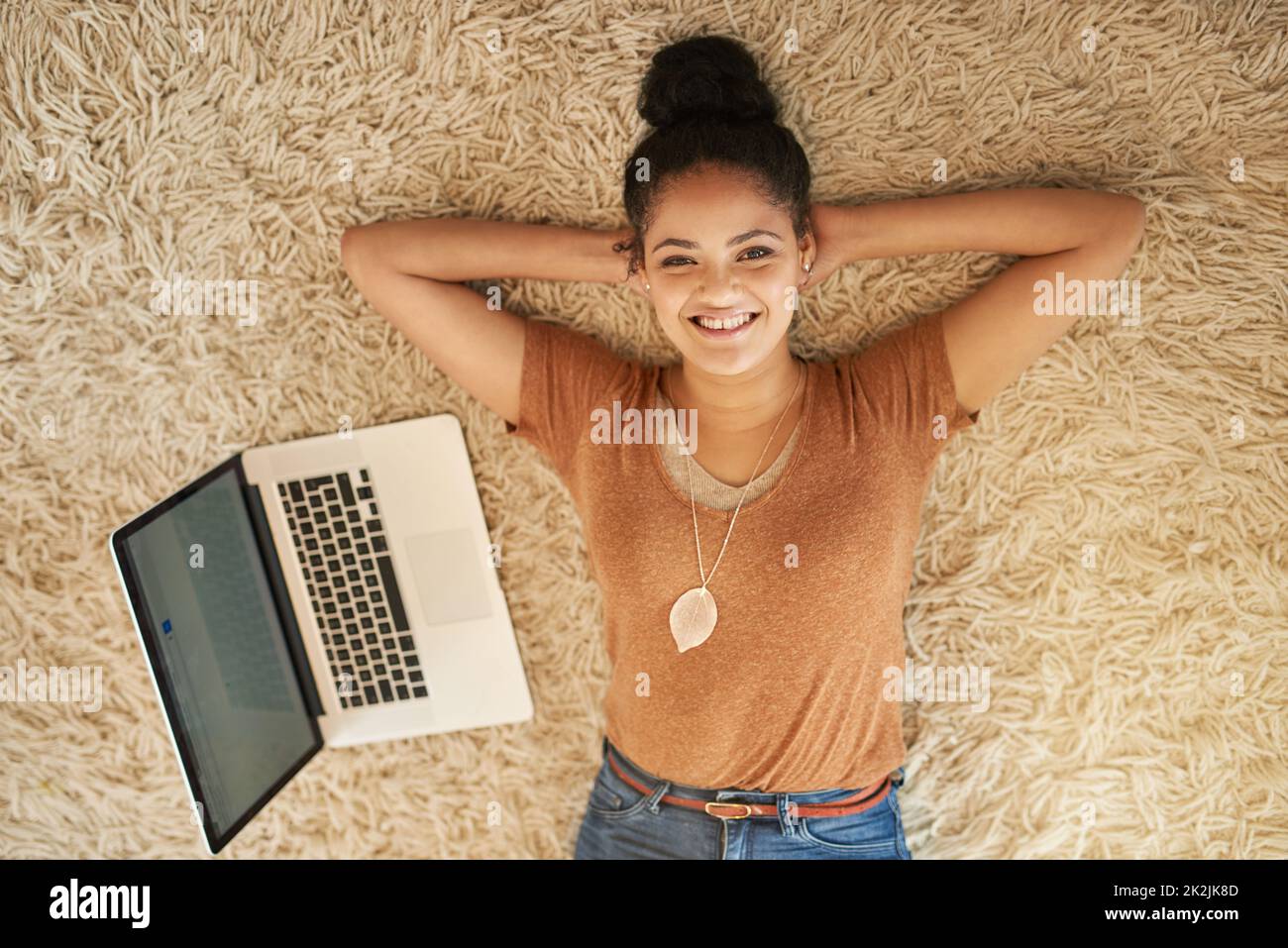 Some relaxation before I go back to online shopping. Shot of a beautiful young woman lying down next to a laptop at home. Stock Photo