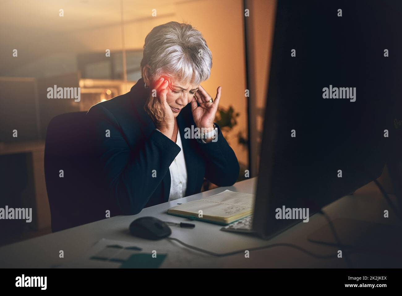 When stress invades the work space. Shot of a mature businesswoman experiencing a headache during a late night at work. Stock Photo
