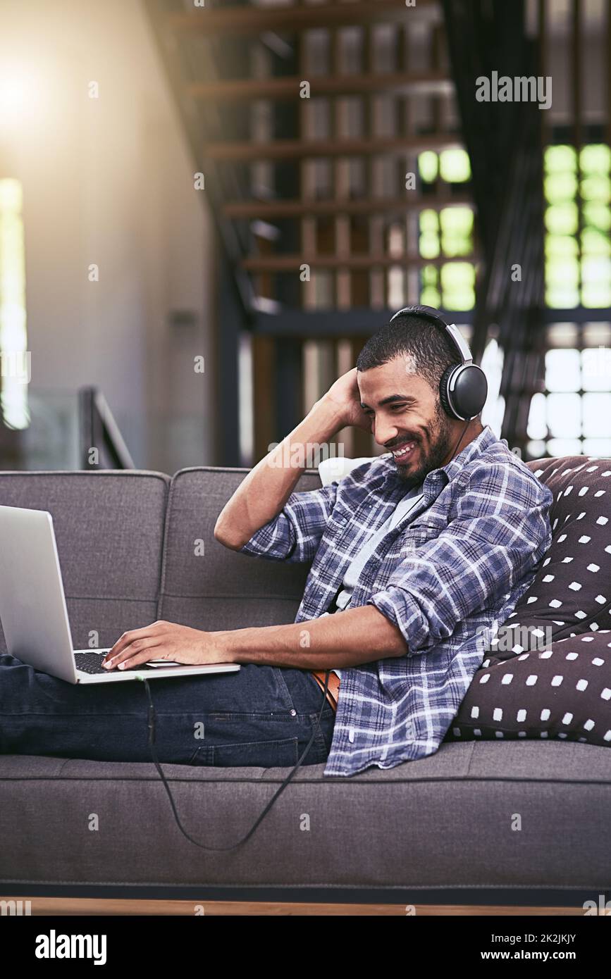 Thats my jam. Shot of a young man using a laptop and headphones on the sofa at home. Stock Photo