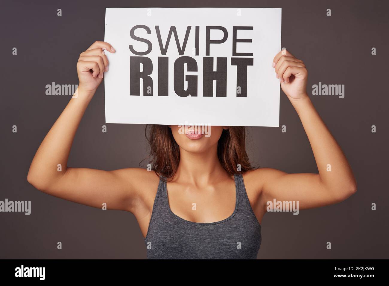 It could be love at first swipe. Studio shot of a young woman holding a sign with swipe right printed on it against a gray background. Stock Photo