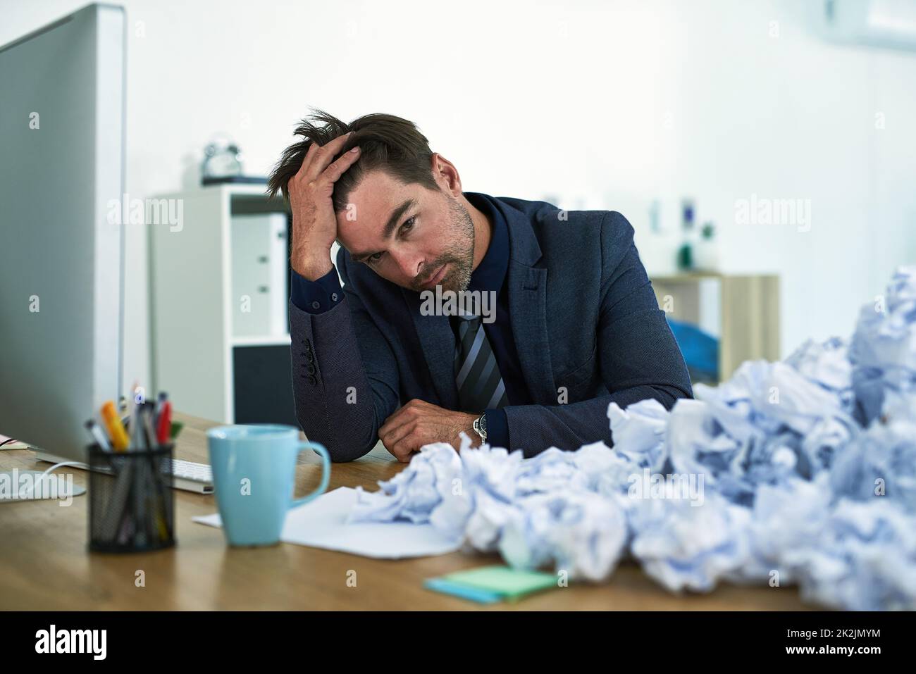 Work just keeps piling up. Shot of a stressed out businessman sitting at his desk overwhelmed by paperwork. Stock Photo