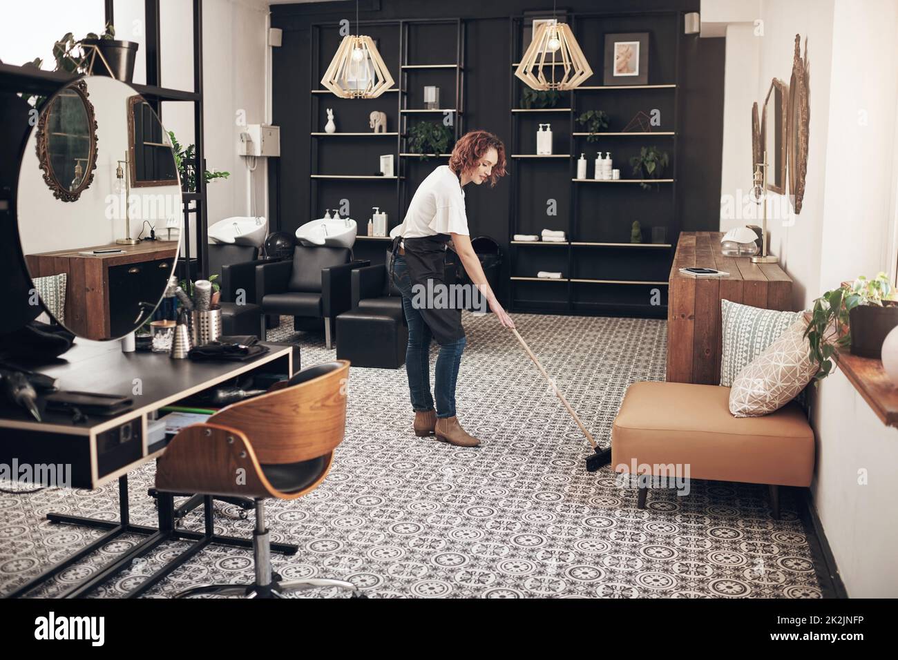 A clean space is a happy space. Shot of a hairstylist sweeping the salon. Stock Photo